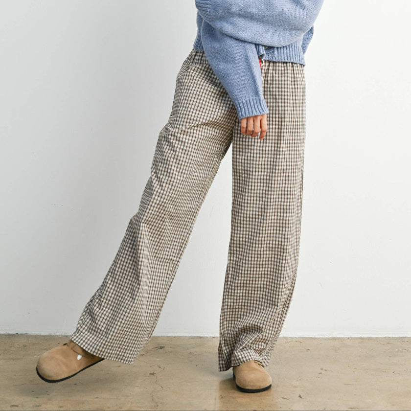 Woman wearing a blue sweater with red accents and plaid pants against a white background