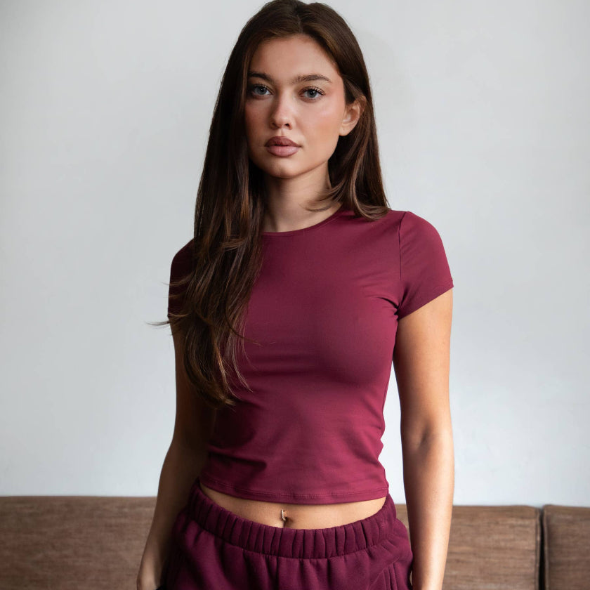 Woman wearing a maroon outfit standing against a neutral background