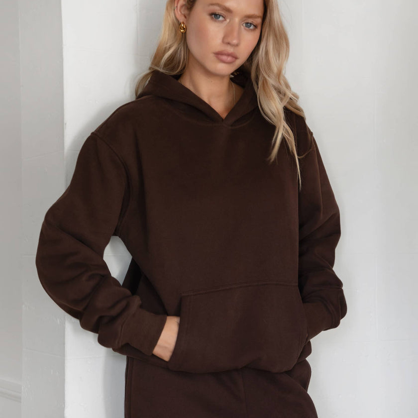 Woman wearing a brown hoodie and pants against a white background