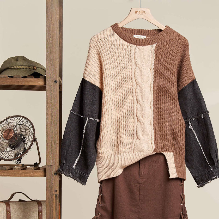Mannequin wearing a brown and beige sweater with black sleeves, standing next to vintage suitcases and a wooden shelf.
