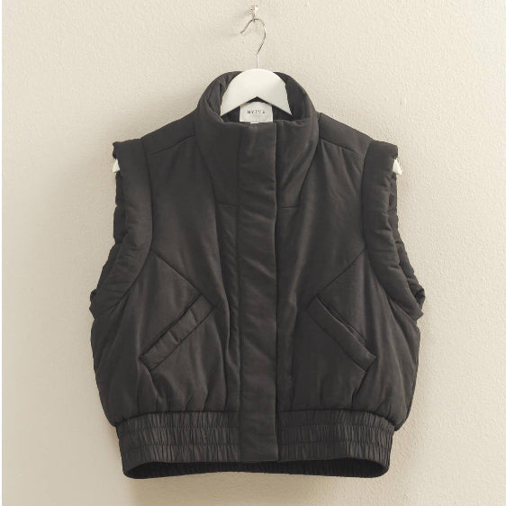 Black puffer vest on a hanger against a beige wall