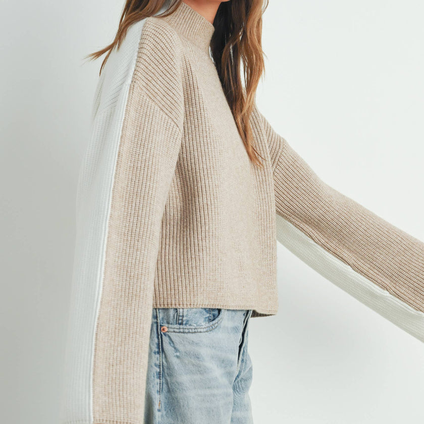 Woman wearing a beige sweater and light blue jeans against a white background
