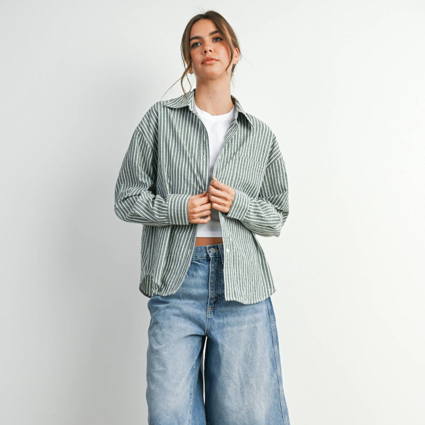 Person wearing a striped shirt, white t-shirt, blue denim shorts, and gold sneakers on a plain background