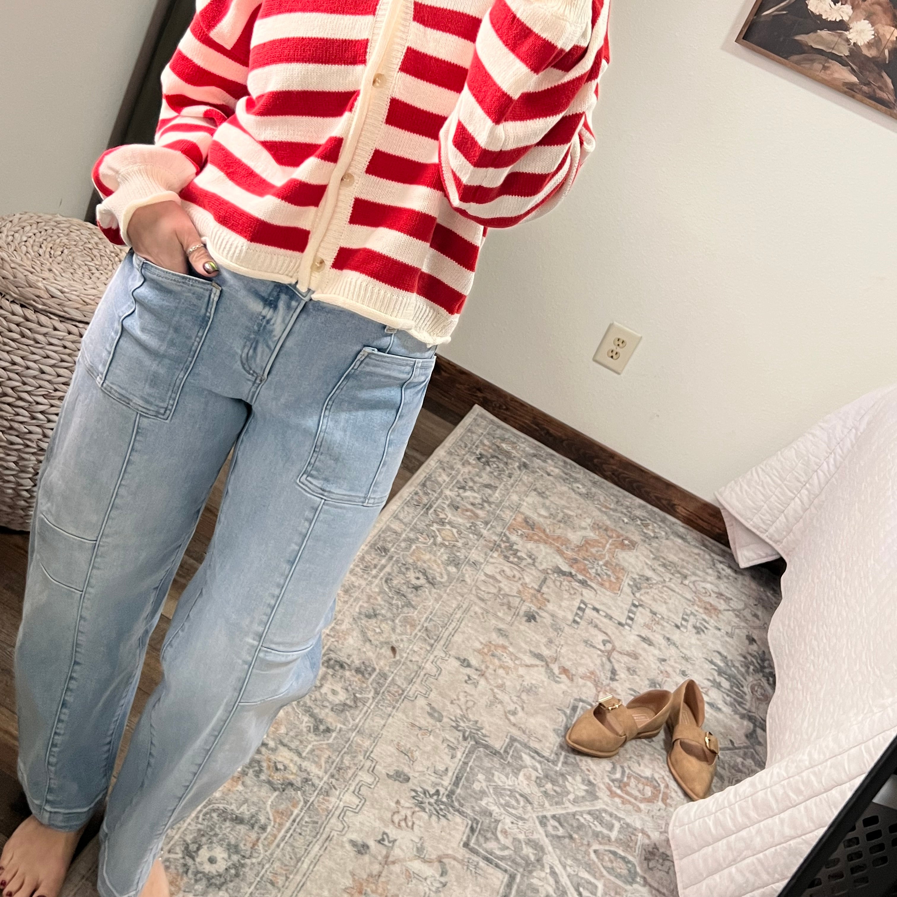 Person wearing a red and white striped shirt and blue jeans in a room with a rug and shoes.