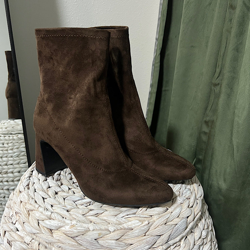 Brown suede ankle boots on a woven stool with a green curtain in the background