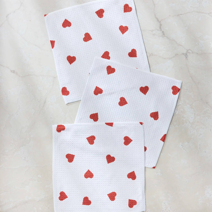 Three white towels with red heart patterns on a light marble background