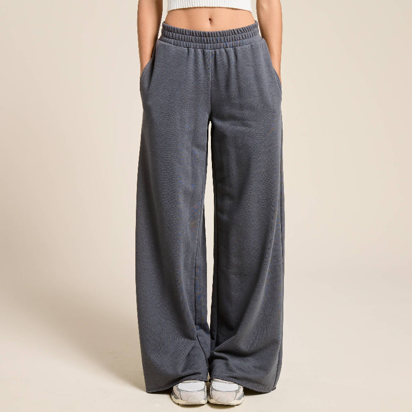 Woman wearing a white sleeveless top and gray wide-leg pants on a beige background