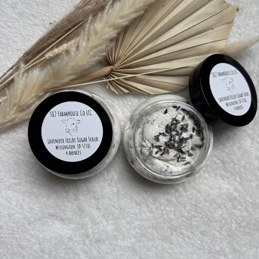 Two small containers of lavender-filled sugar scrub with a dried leaf on a light gray background