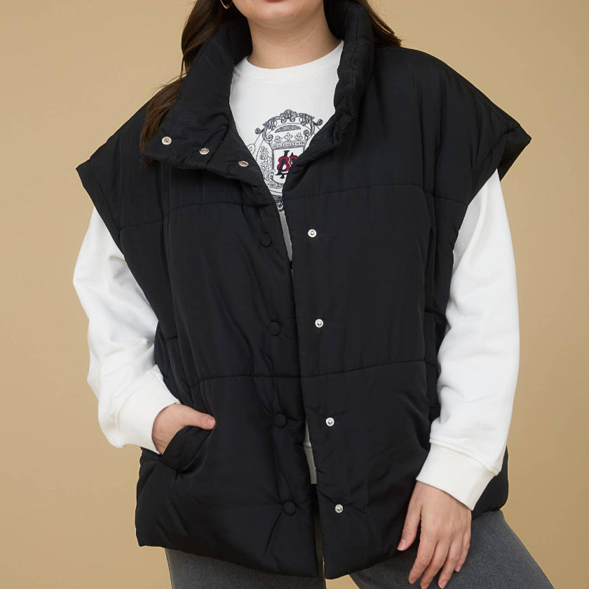 Woman wearing a black puffer vest over a white shirt on a beige background