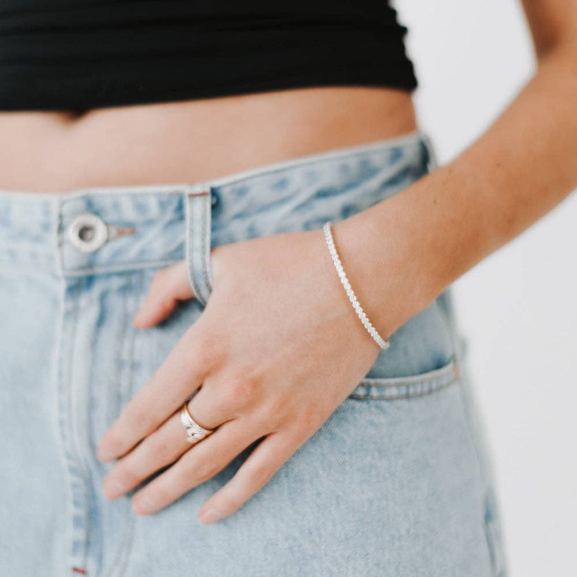 Person wearing a silver bracelet and ring, with light blue jeans.