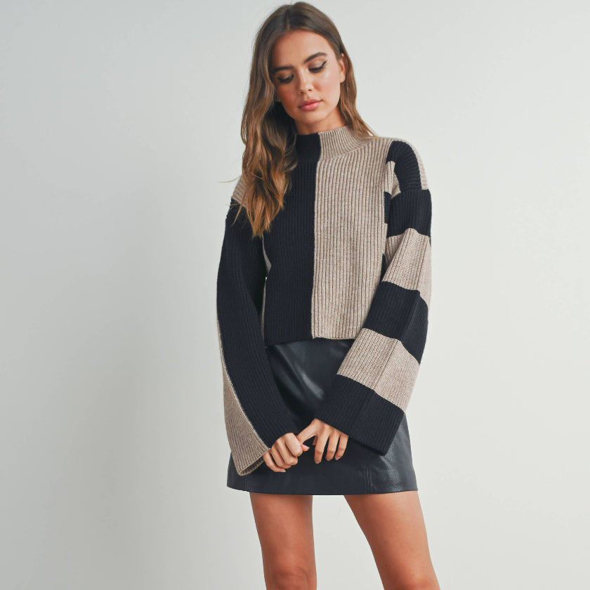 Woman wearing a black and beige sweater dress with knee-high boots on a plain background