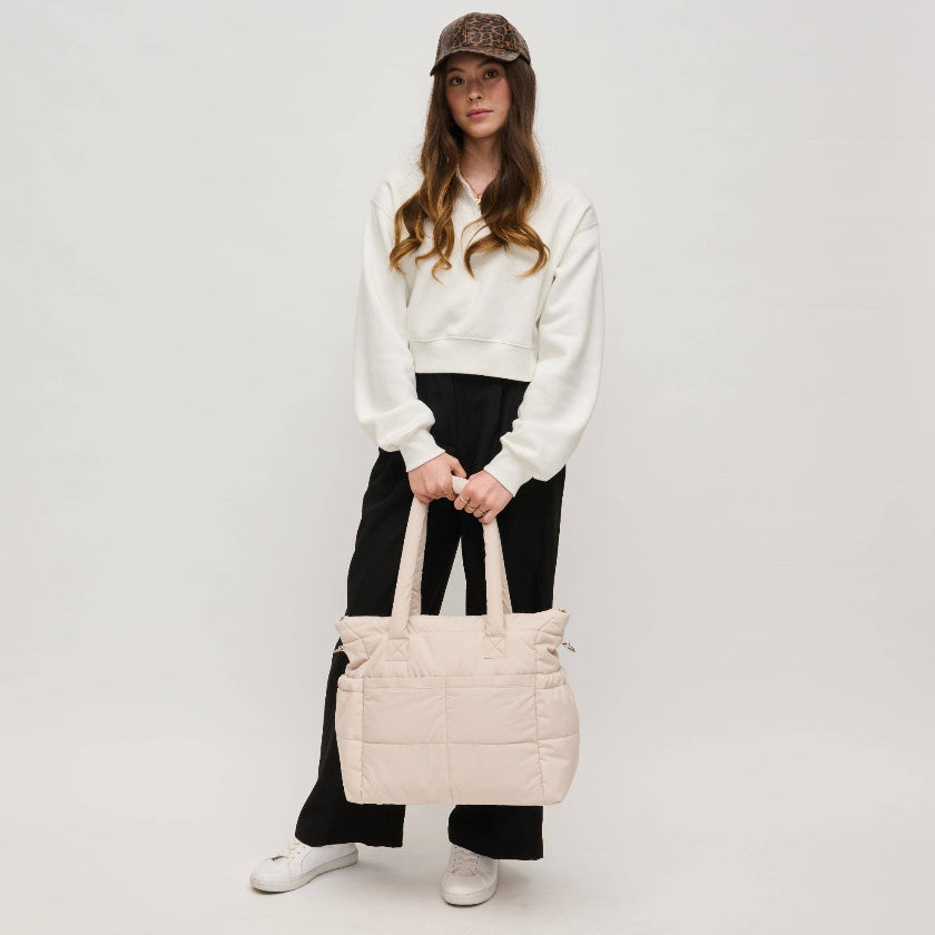 Person holding a beige quilted bag against a plain background