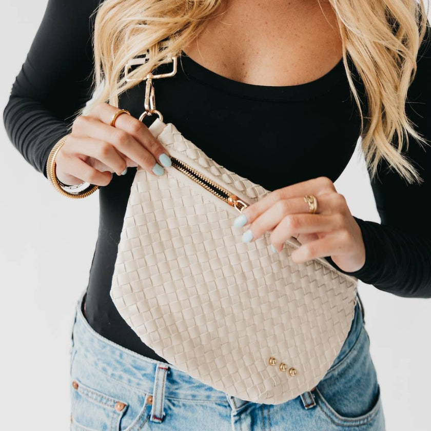 Person holding a beige textured handbag with gold accents on a plain background