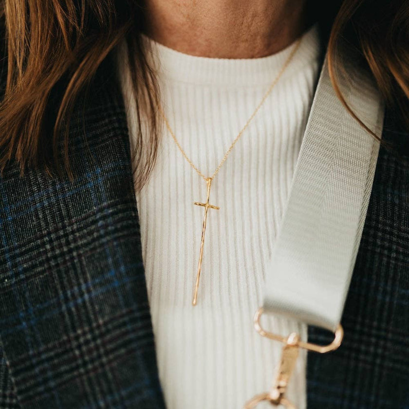 Person wearing a gold cross necklace with a blurred background