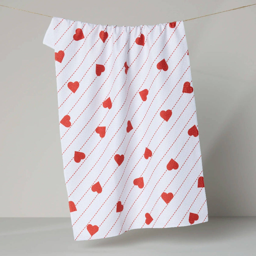White towel with red heart pattern hanging on a line against a plain background