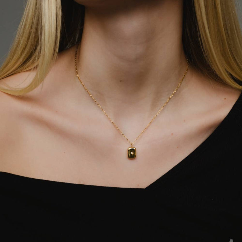 Gold necklace with a small pendant on a plain background