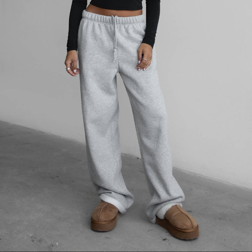 Woman wearing a black long-sleeve top and gray sweatpants against a plain background