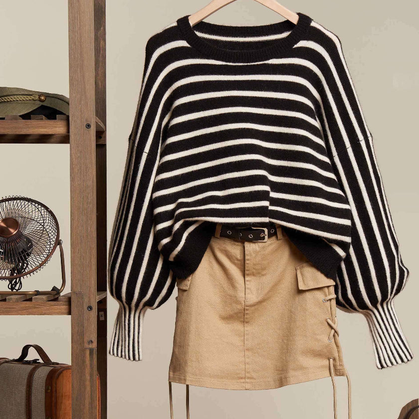 Black and white striped sweater with beige shorts and brown boots on a hanger against a neutral background.