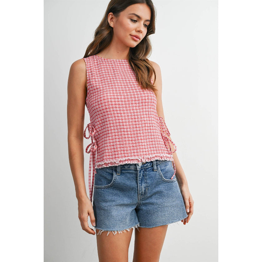 Woman wearing a red and white checkered sleeveless top and denim shorts on a light gray background