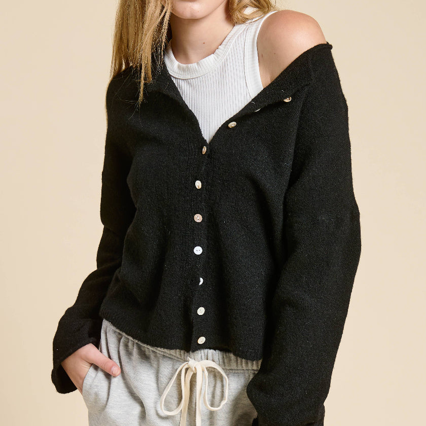 Woman wearing a black cardigan over a white top and light gray pants on a beige background