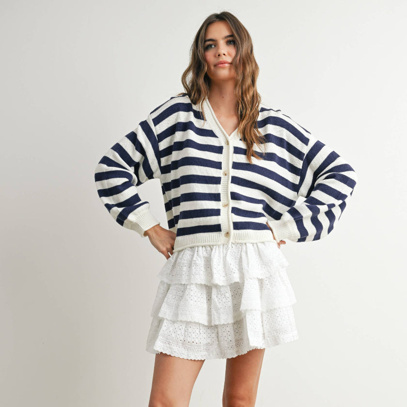 Woman wearing a navy and white striped cardigan over a white top and shorts, standing against a plain background.