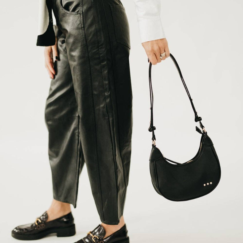 Person wearing black leather pants and holding a black handbag on a white background