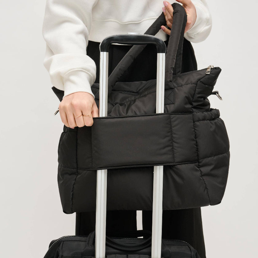 Person holding a black puffer bag over a suitcase on a light gray background