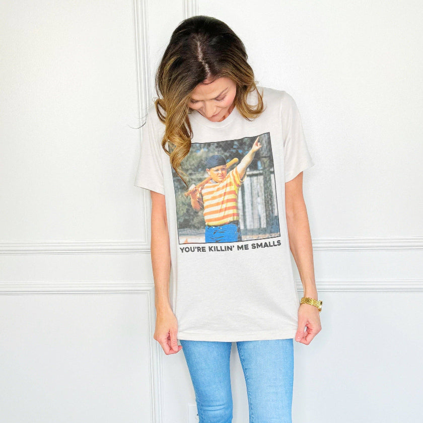 Woman wearing a white t-shirt with a graphic and text, standing against a white wall.
