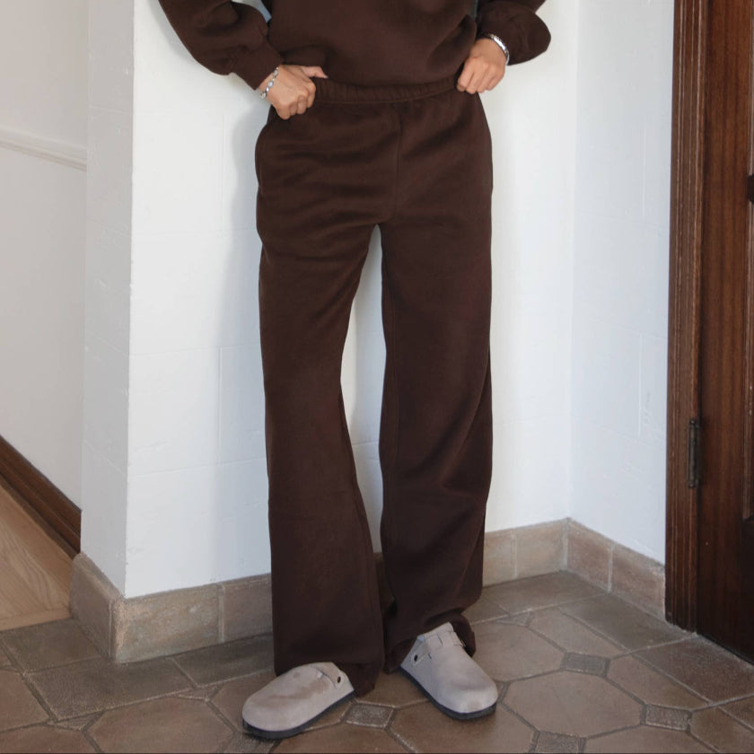 Woman wearing a brown outfit standing against a white wall.