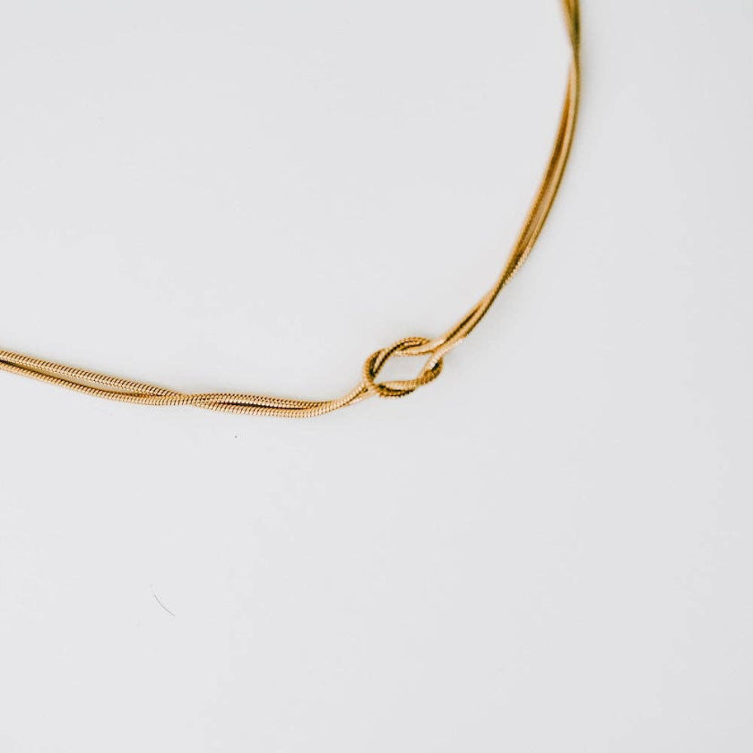 Gold necklace with a knot design on a white background