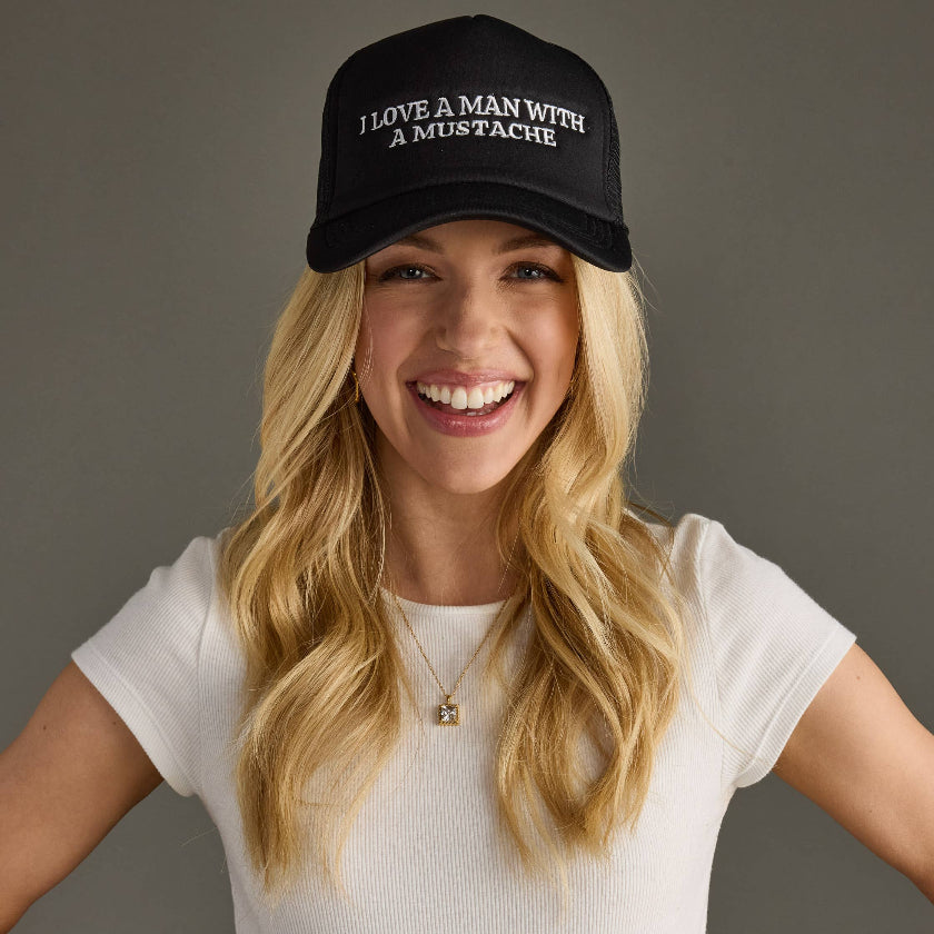 Woman wearing a black cap with text, smiling against a gray background