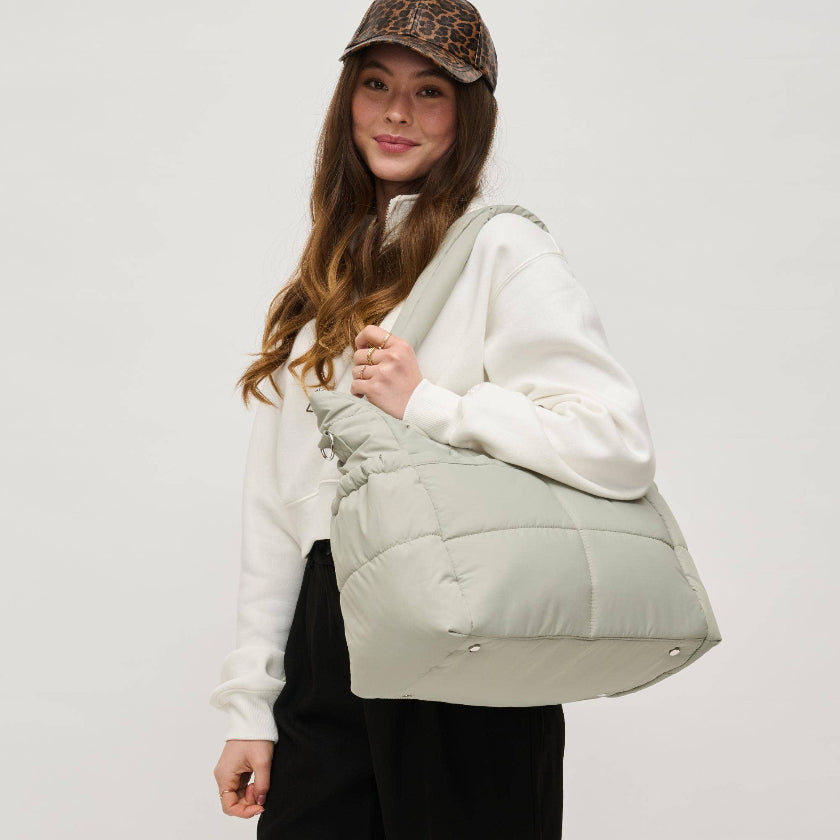 Woman holding a light green quilted bag against a plain background
