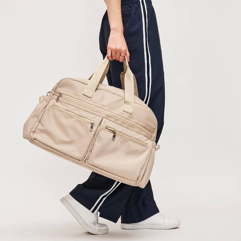 Person holding a beige duffel bag against a plain background