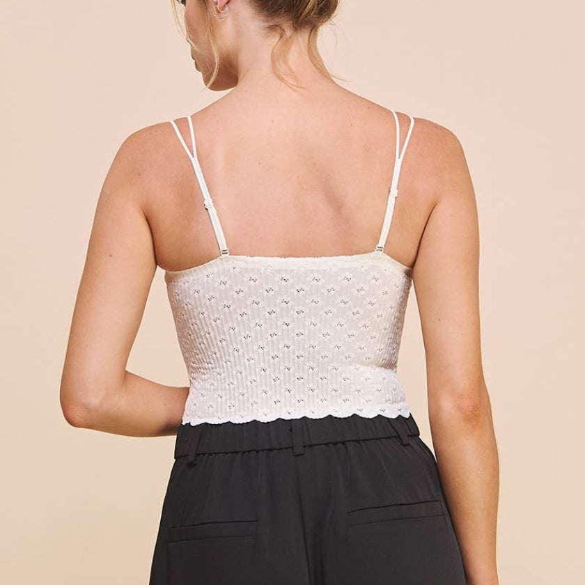 Woman wearing a white textured tank top and black pants on a beige background