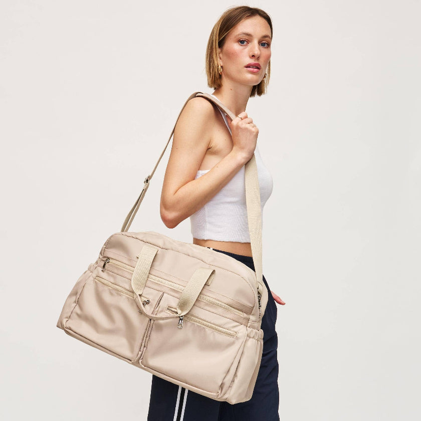 Woman holding a beige duffel bag against a plain background