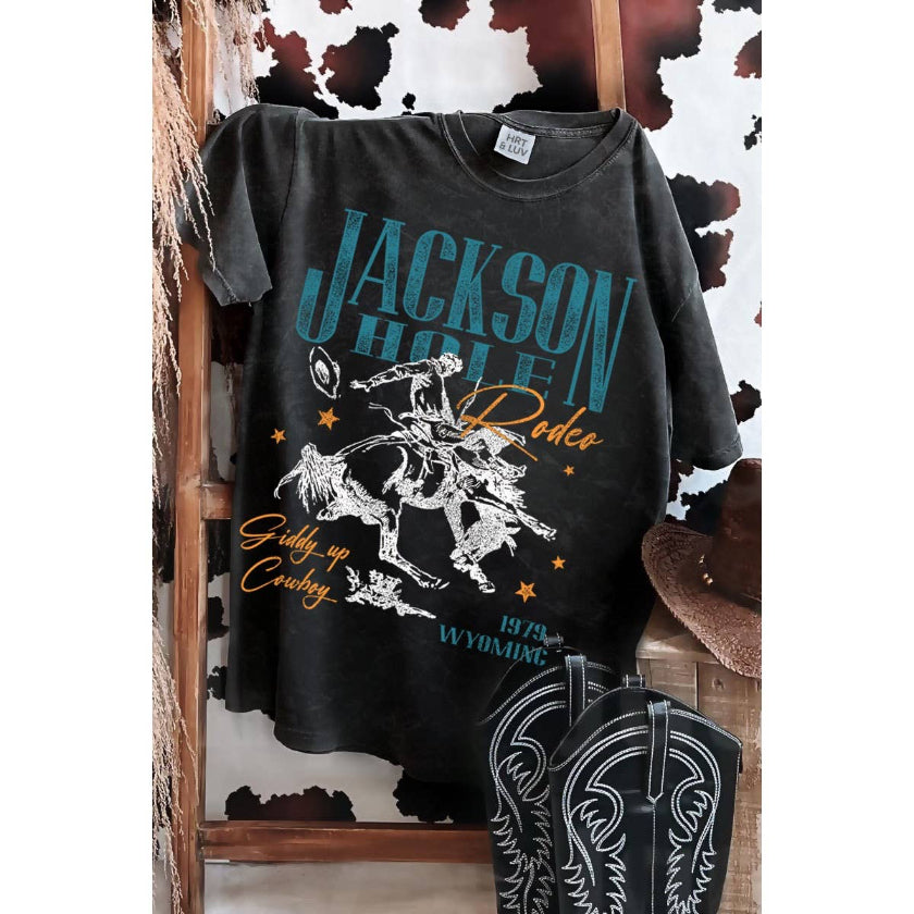 Black t-shirt with 'Jackson Hole Rodeo' design on a wooden stand with cowboy hat and boots.
