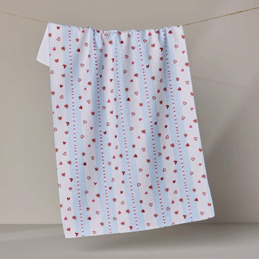 Fabric with red heart patterns on a light blue background, hanging against a beige wall.