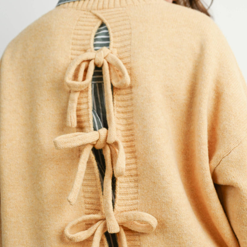 Woman wearing a beige cardigan with bow details on a plain background