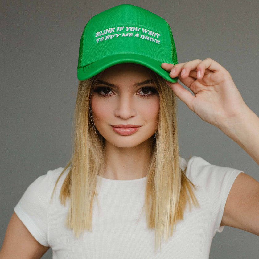 Woman wearing a green cap with text, posing against a gray background