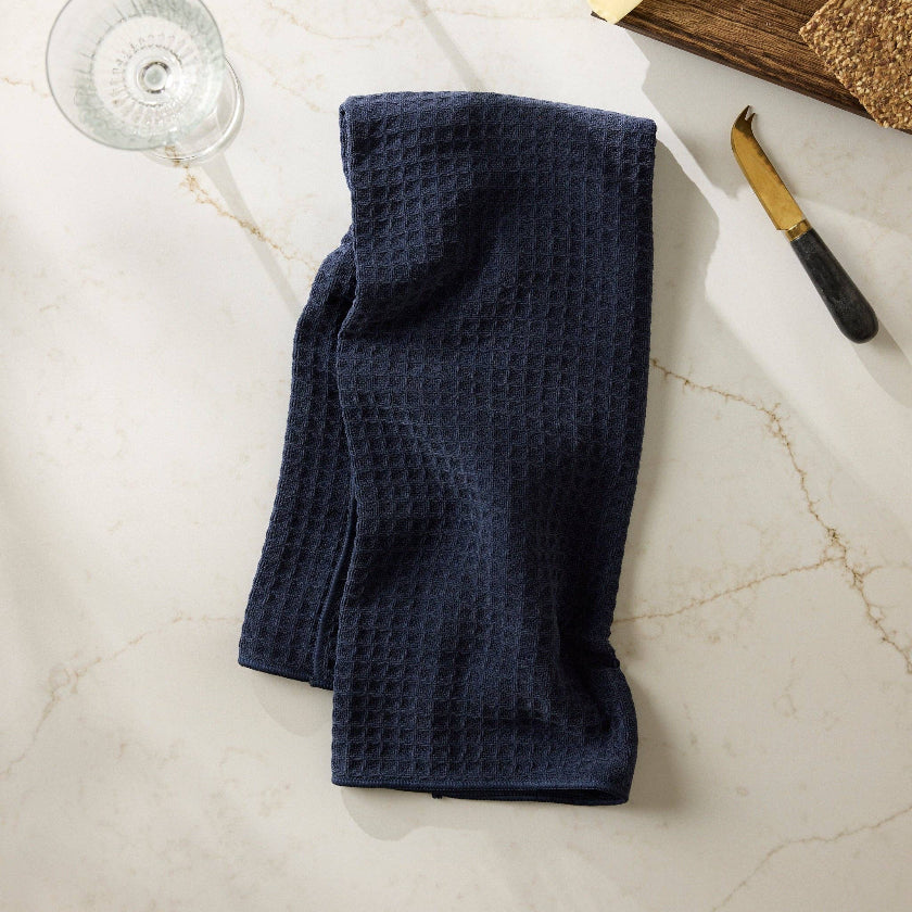 Navy blue waffle-textured towel on a marble surface with glasses, cheese, and knife.