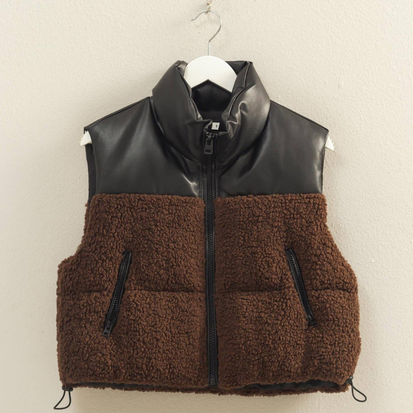 Brown puffer vest with black leather accents on a hanger against a beige wall.
