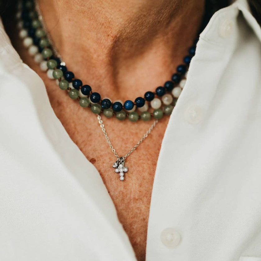Close-up of a person wearing two necklaces with a white shirt.