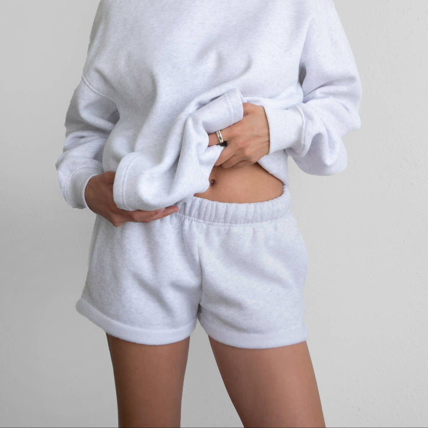 Woman wearing a white hoodie and shorts set on a plain background