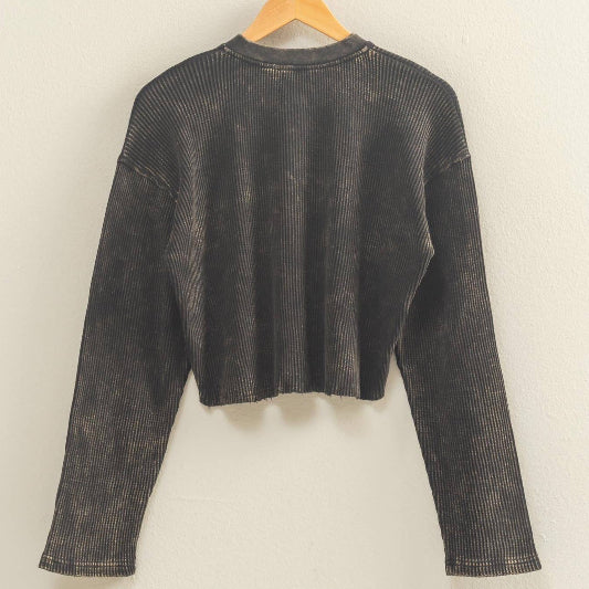Black long-sleeve crop top on a wooden hanger against a beige wall