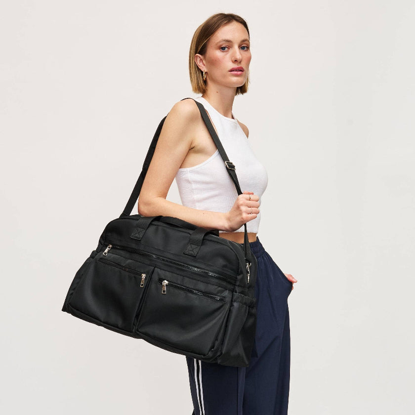 Woman holding a black duffel bag against a plain background