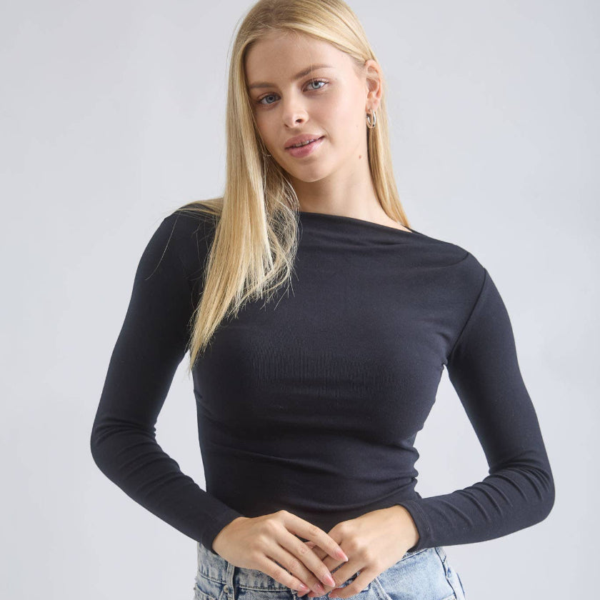 Woman wearing a black long-sleeve top and denim skirt against a plain background