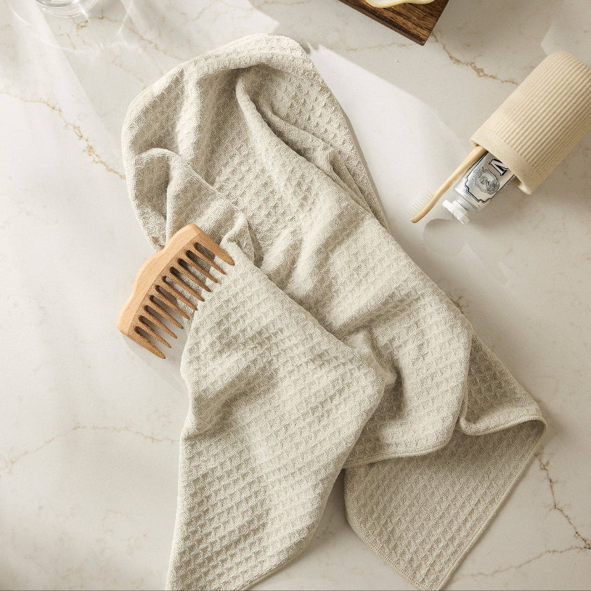 Beige towel draped over a wooden comb on a marble surface with a bottle of lotion and soap dish.