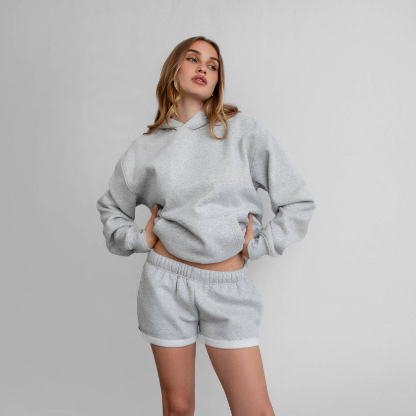 Woman wearing a gray sweatshirt and shorts set on a plain background