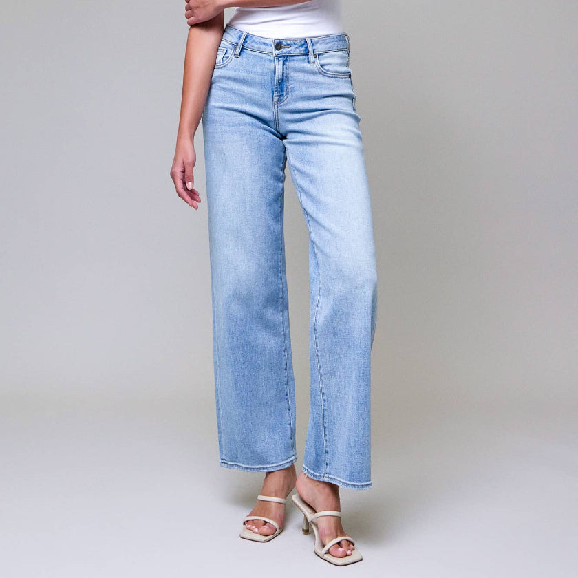 Woman wearing light blue jeans and a white top against a plain background