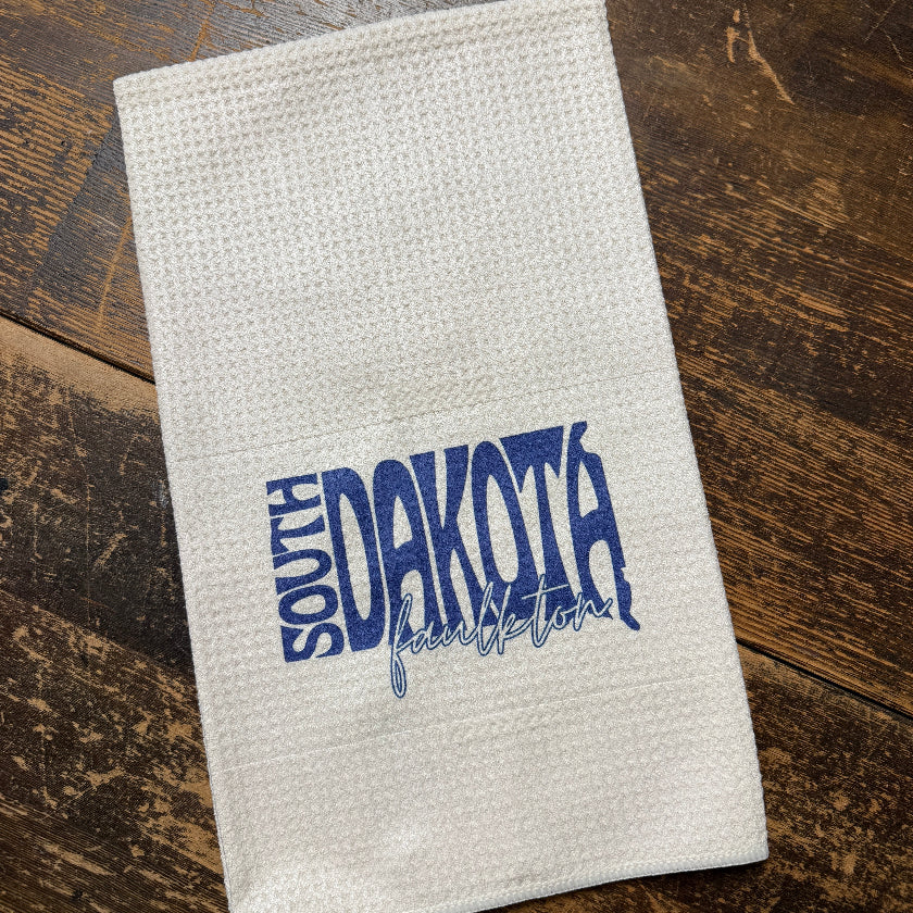 White towel with blue text 'South Dakota' on a wooden surface